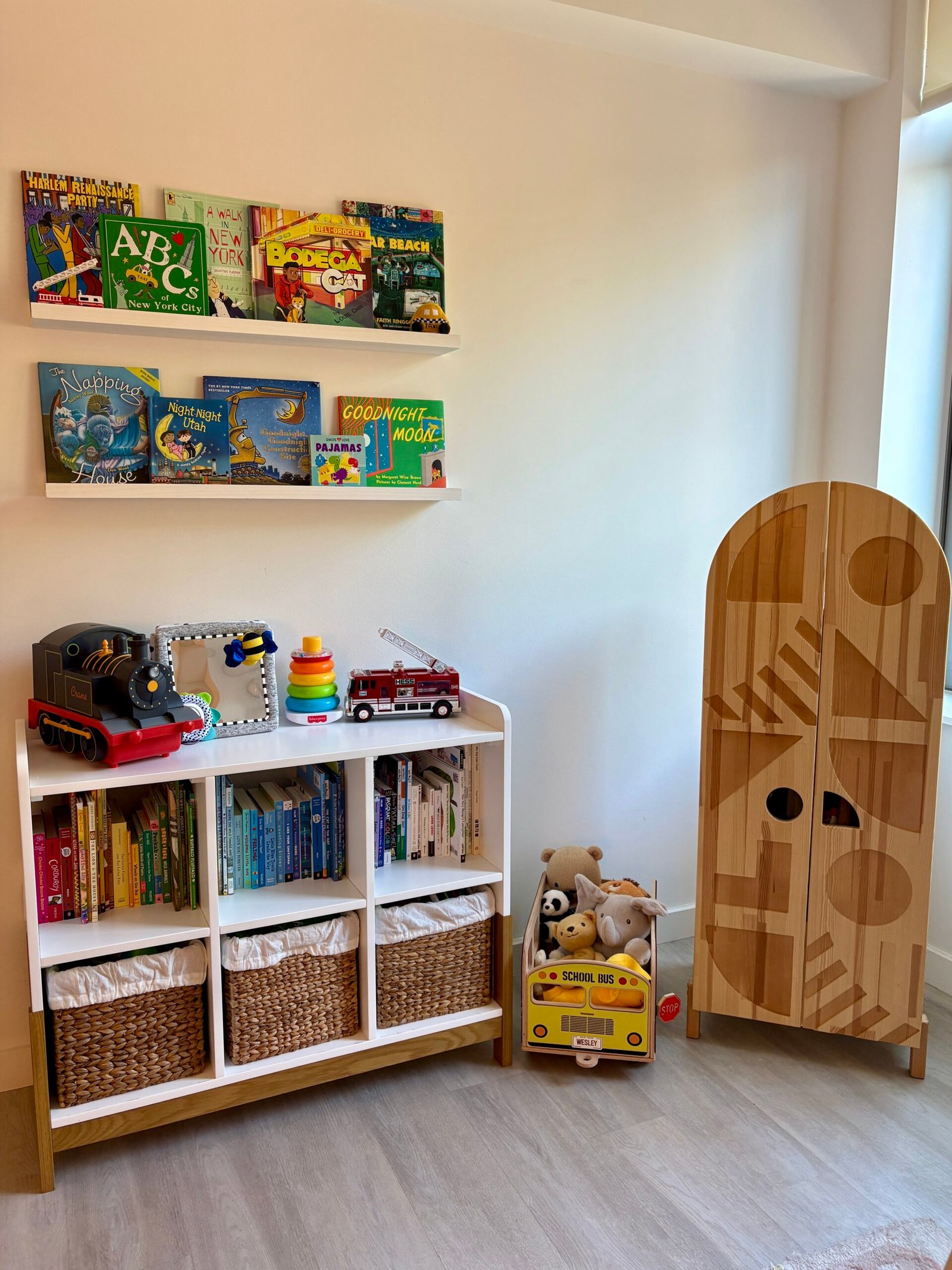 Bright nursery furniture with a wooden bookshelf beside a wardrobe for infant clothing.